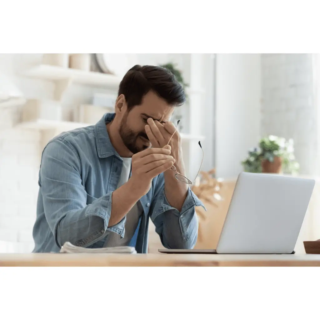 Man rubbing his eyes at a computer.